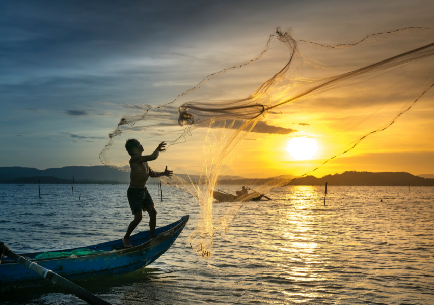 Fisherman casting net into the tropical ocean water with the sun setting in the background